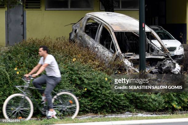 Cyclist rides past the wreckage of a burnt-out car in the Bellevue neighborhood in Nantes on July 6 following another night of violence in the...
