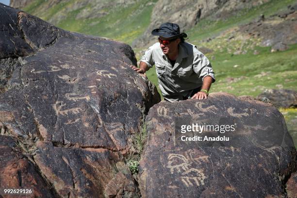 Visitor stands behind petroglyphs, depicting animals, humans along with other symbols on a rock found close to the summit of Mount Cilo in Yuksekova...