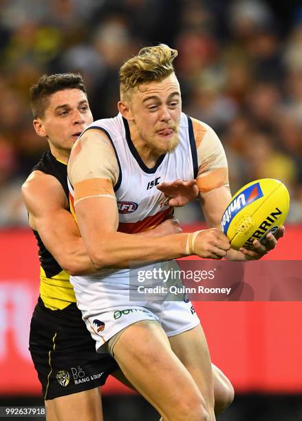 Hugh Greenwood of the Crows handballs whilst being tackled by Dion Prestia of the Tigers during the round 16 AFL match between the Richmond Tigers...