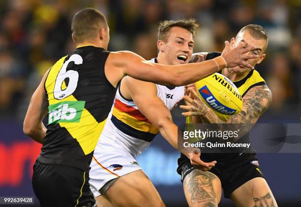 Tom Doedee of the Crows handballs whilst being tackled by Dustin Martin of the Tigers during the round 16 AFL match between the Richmond Tigers and...
