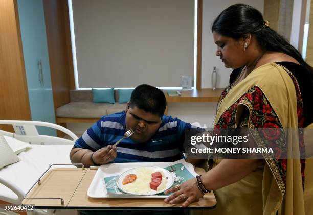 Obese Indian teen Meher Jain eats food as his mother Pooja Jain watches in his hospital room in New Delhi on July 6, 2018. - Meher underwent a...