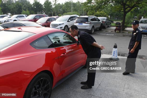 Security guards look at a Ford Mustang outside a dealership in Beijing on July 6, 2018. - China said on July 6 it was "forced to take necessary...