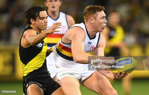 Tom Lynch of the Crows handballs whilst being tackled by Daniel Rioli of the Tigers during the round 16 AFL match between the Richmond Tigers and the...