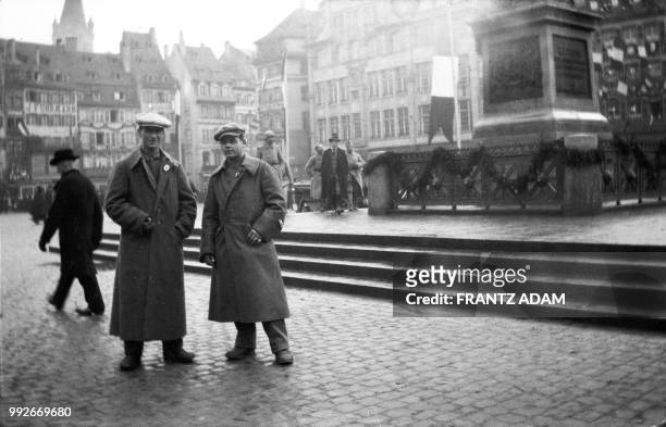 Two young men wearing long coats stand at Kleber Square decorated with flags in Strasbourg, eastern France, on December 1, 1918. The Allied troops...