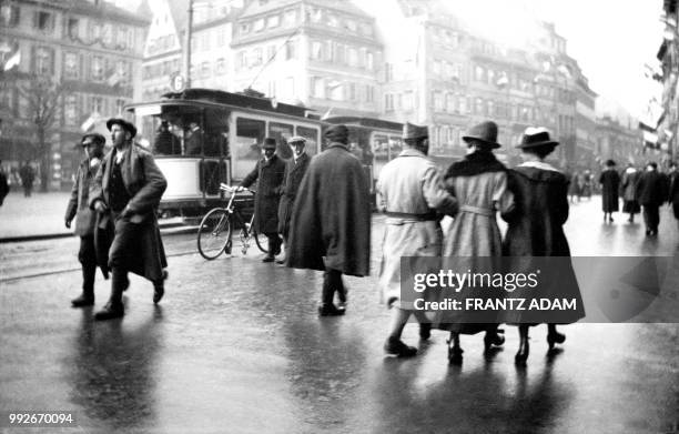 French soldier walks arm in arm with two women on a boulevard decorated with flags in Strasbourg, eastern France, on December 1, 1918. They pass in...