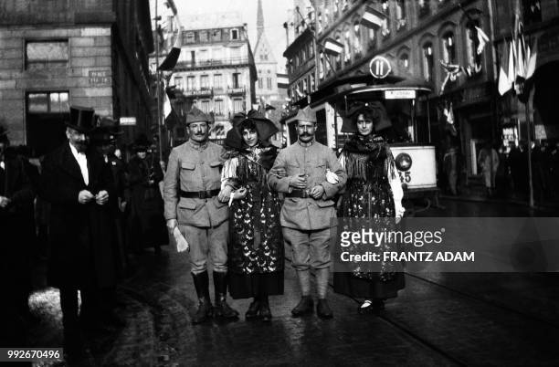 Two French uniformed soldiers pose arm in arm with two young women dressed in traditionnal Alsacian costume in a street decorated with flags in...