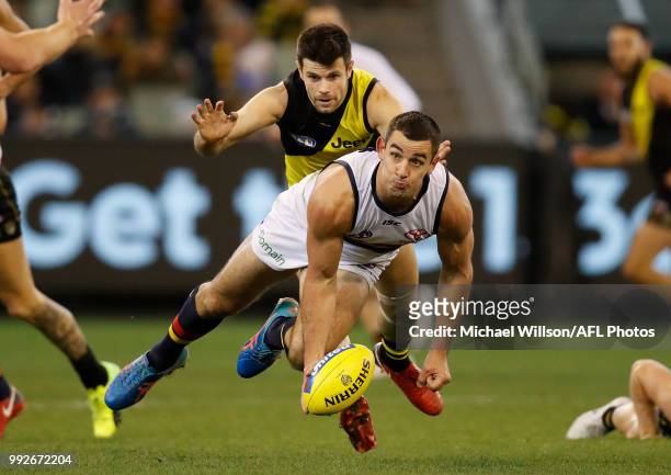 Taylor Walker of the Crows passes the ball under pressure of Trent Cotchin of the Tigers during the 2018 AFL round 16 match between the Richmond...