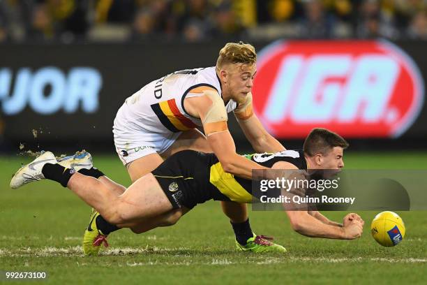 Jack Higgins of the Tigers handballs whilst being tackled by Hugh Greenwood of the Crows during the round 16 AFL match between the Richmond Tigers...