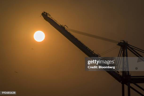 The sun sets behind a gantry crane at the Port of Oakland in Oakland, California, U.S., on Tuesday, July 3, 2018. President Donald Trump threatened...