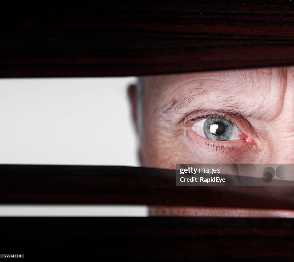 Mature man looking through venetian blinds, frowning