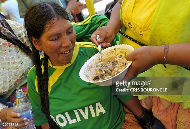 An Bolivian Andean peasant woman wearing a T-shirts with the name of her country eats a typical Cahiro Paceno, a hearty soup, before an encounter...