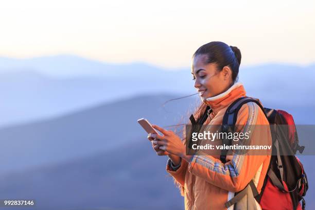 smiling female hiker using smart phone on top mountain - asian woman smiling sunrise stock pictures, royalty-free photos & images