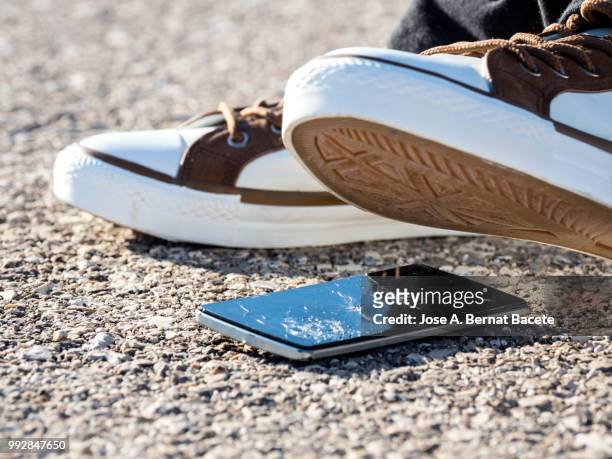 slipper of white color of a person squishing a mobile phone against the soil, outdoors. - crushed photos et images de collection