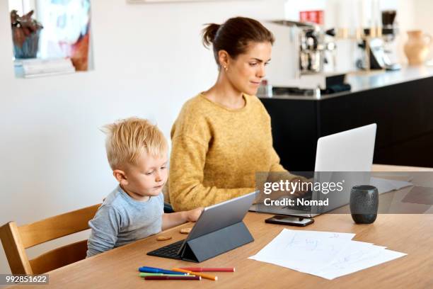 mother and son using technologies at table - mother and son using tablet and laptop stock pictures, royalty-free photos & images