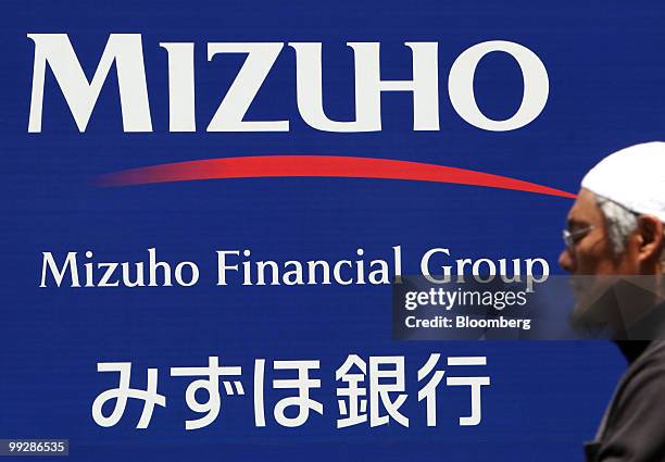 Pedestrian walks past sign for Mizuho Bank Ltd. Displayed outside one of their branches in Tokyo, Japan, on Friday, May 14, 2010. Mizuho Financial...