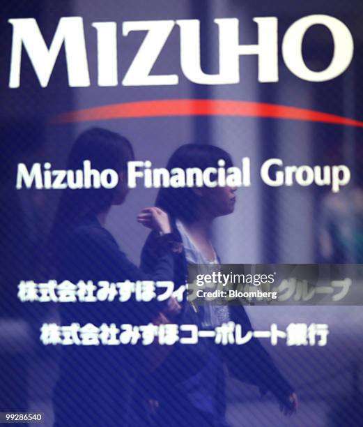 Pedestrians are reflected in a sign for Mizuho Financial Group Inc. Outside the company's headquarters in Tokyo, Japan, on Friday, May 14, 2010....