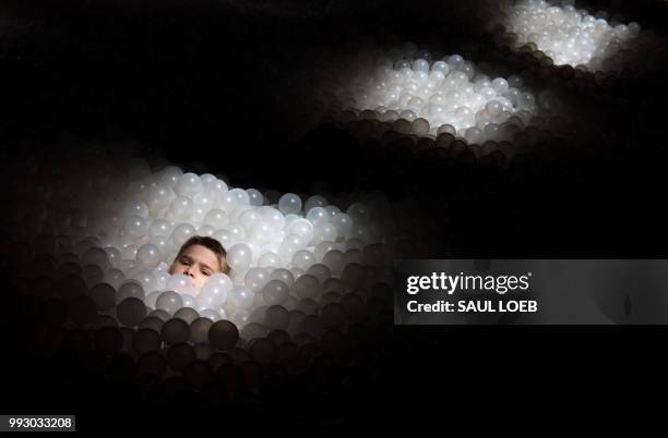 Boy plays in a "swimming pool" filled with plastic balls at the Fun House exhibit, a freestanding structure designed by Snarkitecture that recalls...