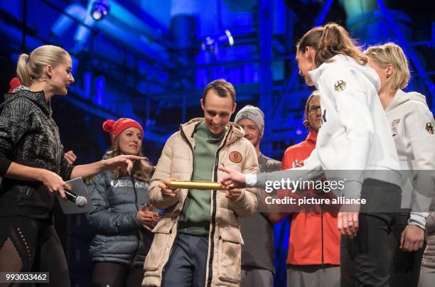 The German combiner Eric Frenzel receives a golden relay baton from Beach Volleyball gold medalists Laura Ludwig and Kira Walkenhorst during the...