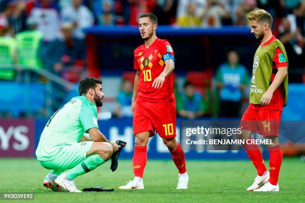 Brazil's goalkeeper Alisson crouches on the field as Belgium's forward Eden Hazard and Belgium's forward Dries Mertens walk past at the end of the...