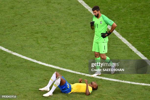 Brazil's midfielder Fernandinho lies on the field as Brazil's goalkeeper Alisson walks past him at the end of the Russia 2018 World Cup quarter-final...