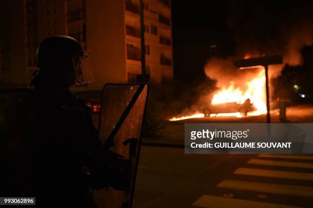 French police officer looks at a burning car in the Le Breil neighborhood of Nantes early on July 7, 2018. - A French policeman who shot dead a young...