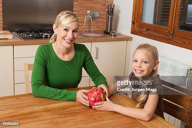 mother and daughter hold a piggy bank - blonde girl piggy bank stock-fotos und bilder