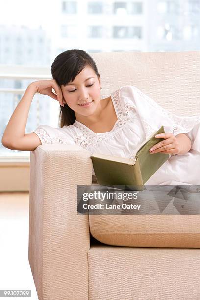 asian woman reading on a sofa - armlehne stock-fotos und bilder