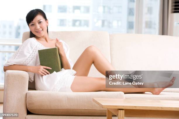 asian woman reading on a sofa - armlehne stock-fotos und bilder