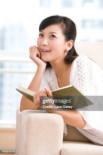 asian woman reading on a sofa - armlehne stock-fotos und bilder