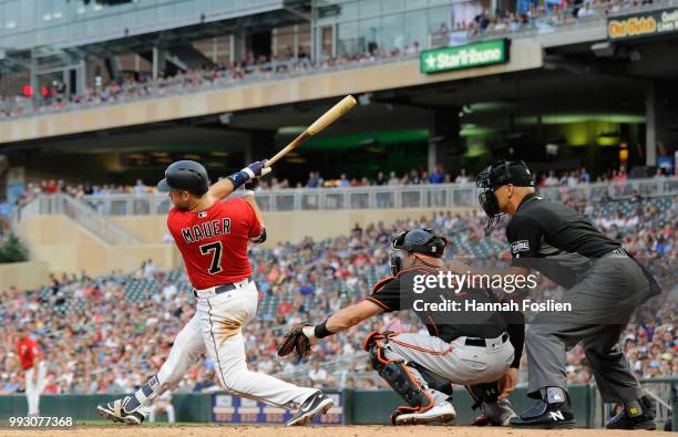 Joe Mauer of the Minnesota Twins hits an RBI single as Caleb Joseph of the Baltimore Orioles catches and umpire Vic Carapazza calls balls and strikes...