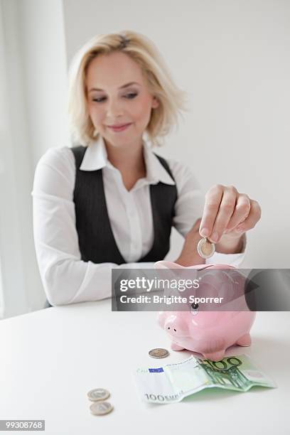 woman dropping money into piggy bank - brigitte sporrer stock pictures, royalty-free photos & images