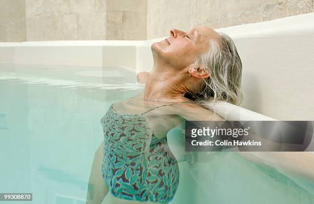 senior woman relaxing in pool - colin hawkins stock pictures, royalty-free photos & images