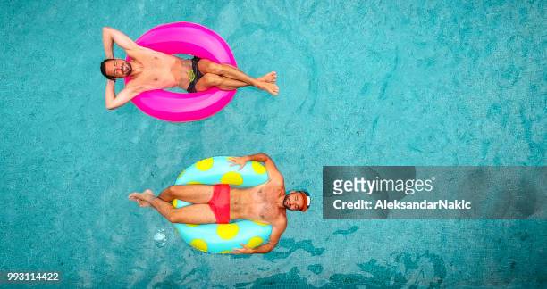 entspannen sie sich auf aufblasbaren ringen zwei mann - aerial pool stock-fotos und bilder