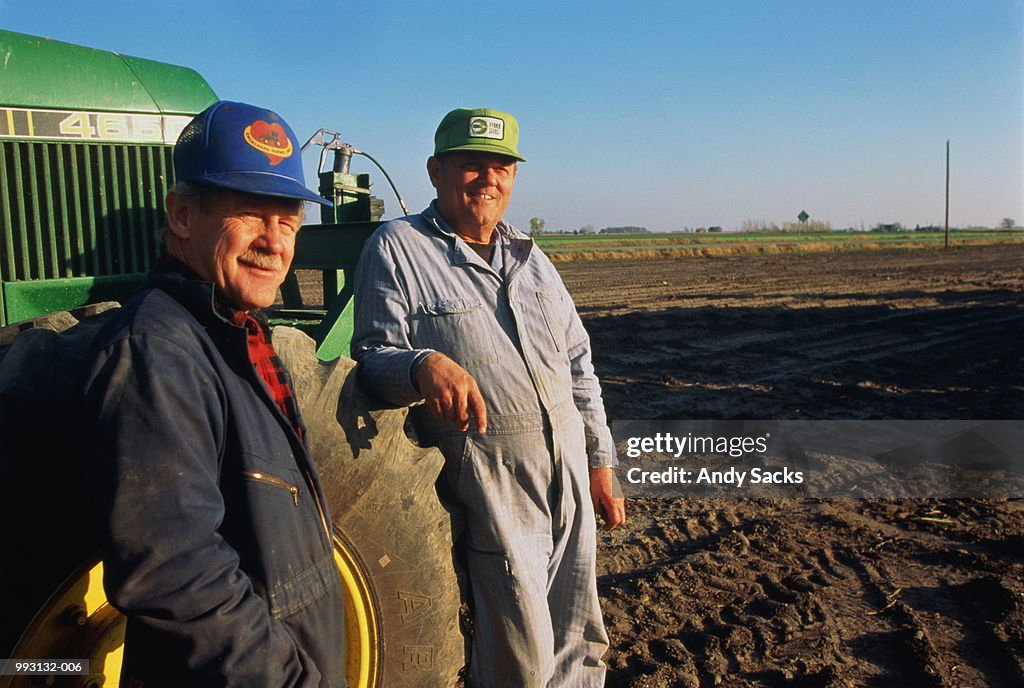 Two farmers standing by tractor in field