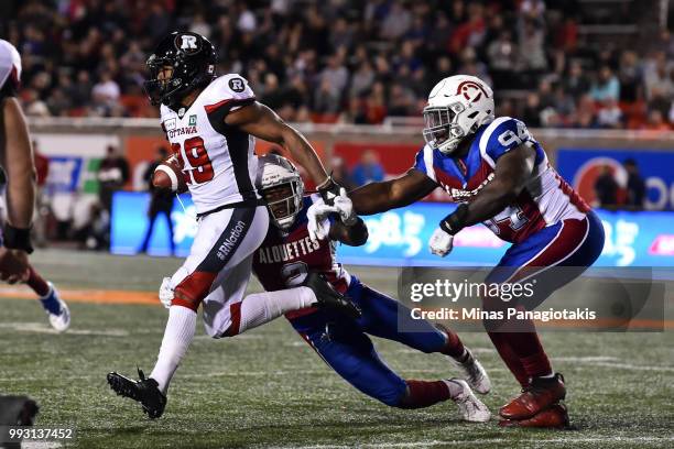 Running back William Powell of the Ottawa Redblacks runs with the ball against defensive back Dominique Ellis and defensive tackle Fabion Foote of...