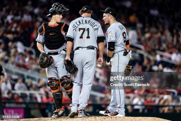 Miguel Rojas and J.T. Realmuto of the Miami Marlins meet with relief pitcher Drew Steckenrider during the eighth inning against the Washington...