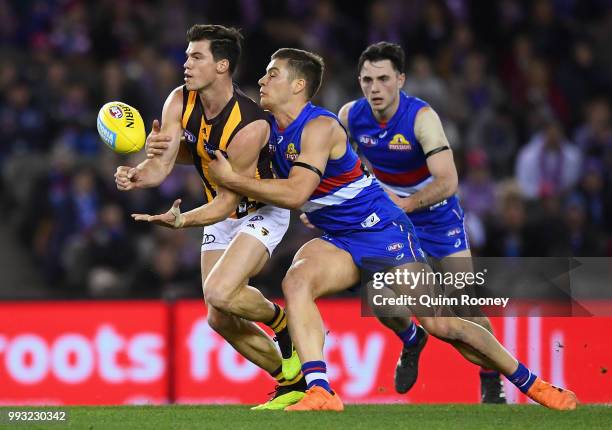 Jaeger O'Meara of the Hawks handballs whilst being tackled by Josh Dunkley of the Bulldogs during the round 16 AFL match between the Western Bulldogs...