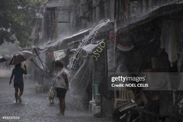 Woman soaks from water coming from the roof's rain gutter in Manila on July 7, 2018. - Health officials have said that the surge in leptospirosis...