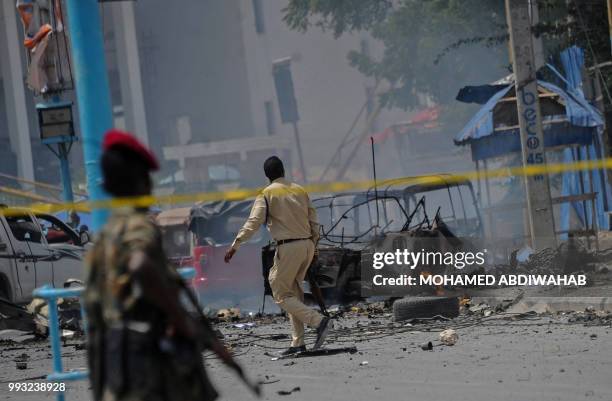 Somali security force personnel look on as the wreckage of a vehicle burns at the site of a car bomb explosion near the building of the Interior...