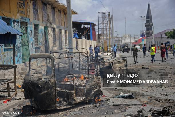 Bystanders and rescue personnel look on as the wreckage of a vehicle burns at the site of a car bomb explosion near the building of the Interior...