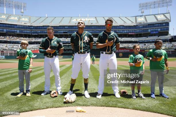 Matt Chapman, Matt Olson and Sean Manaea of the Oakland Athletics stand on the field with little leaguers during the anthem prior to the game against...