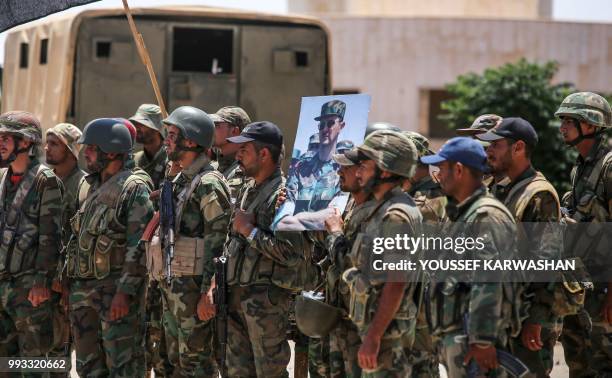 Syrian government soldiers stand holding a picture of Syrian President Bashar al-Assad dressed in a Field Marshal's camouflage fatigues at the Nassib...