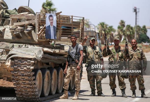 Syrian government soldiers stand flashing the victory gesture next to a picture of Syrian President Bashar al-Assad hanging on a tank at the Nassib...