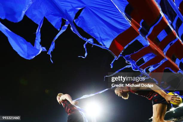 Clayton Oliver of the Demons runs under the banner with Max Gawn of the Demons during the round 16 AFL match between the Melbourne Demons and the...