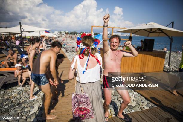 Russian football fans carrying a flag and wearing flowers in their hair walks past a beach fitness class in front of the Fisht stadium prior to the...