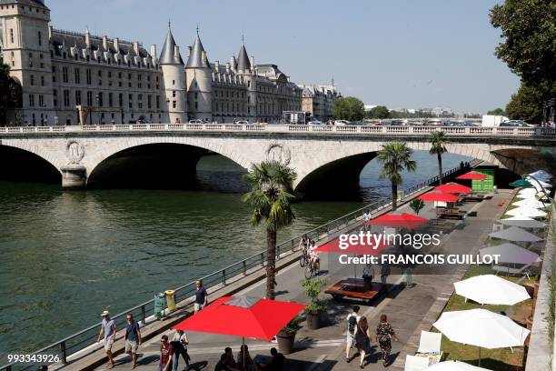 People walk along parasols on the banks of the river Seine near la Conciergerie in Paris on July 7, 2018 during the 17th edition of Paris Plage...