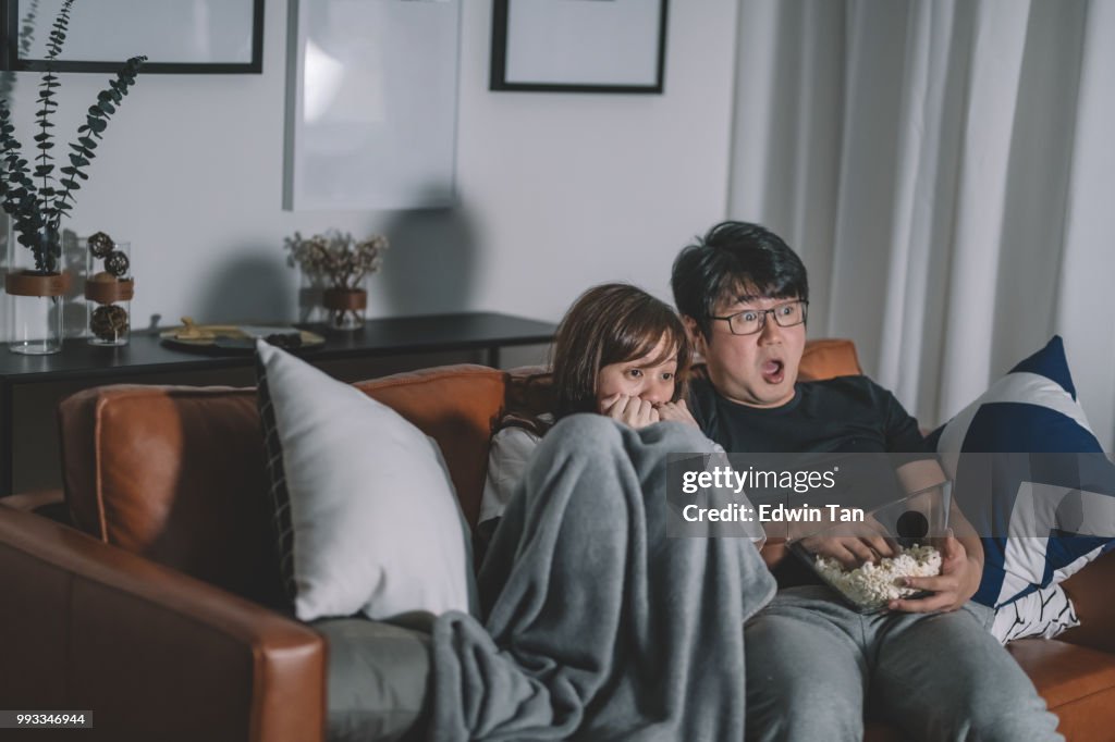 Asiático chino par ver scary horror televisivo en la noche durante fin de semana en la sala de estar sentado en el sofá