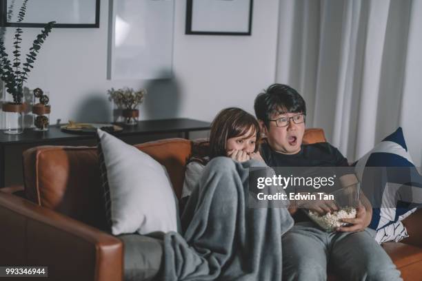 asian chinese couple watching scary horror tv show at night during weekend in living room sitting on sofa - enchanted film stock pictures, royalty-free photos & images