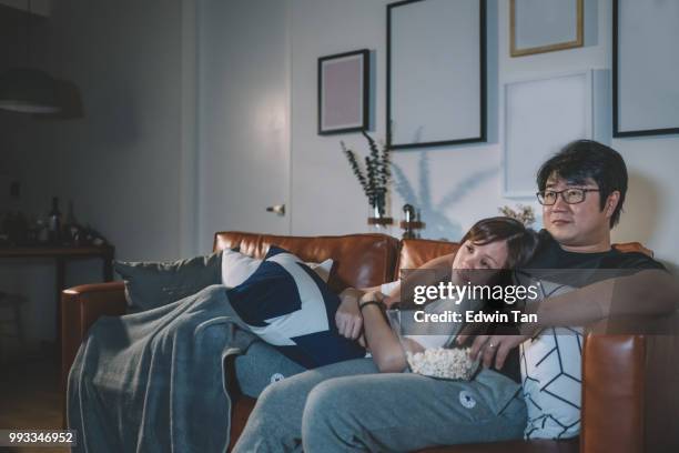 aziatische chinese paar kijken naar tv show op nacht tijdens weekend in woonkamer zittend op de bank - asian watching movie stockfoto's en -beelden