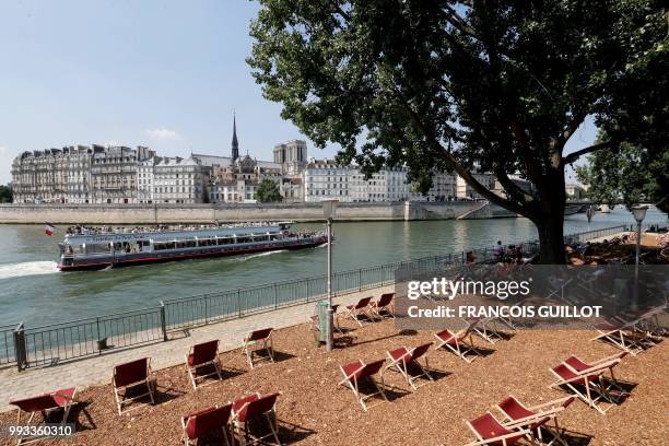 People rest on transat as a bateau-mouche sails on the river Seine near the ile de la Cite in Paris on July 7, 2018 during the 17th edition of Paris...